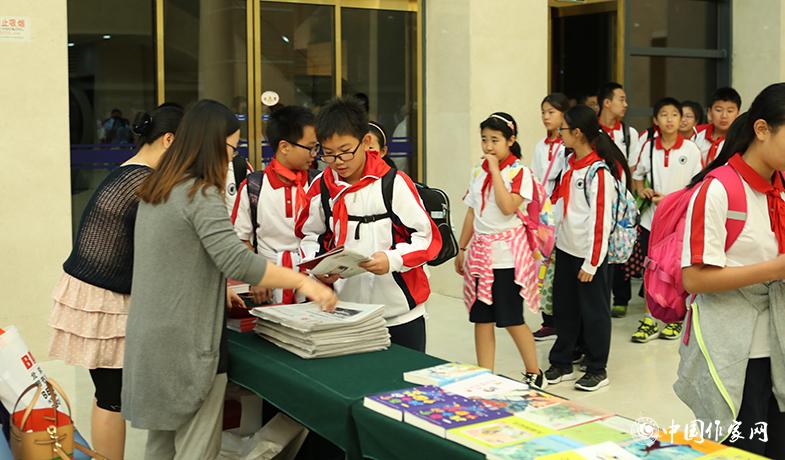 參加頒獎(jiǎng)典禮的學(xué)生排隊(duì)入場，工作人員為他們分發(fā)當(dāng)天的《文藝報(bào)》兒獎(jiǎng)特刊